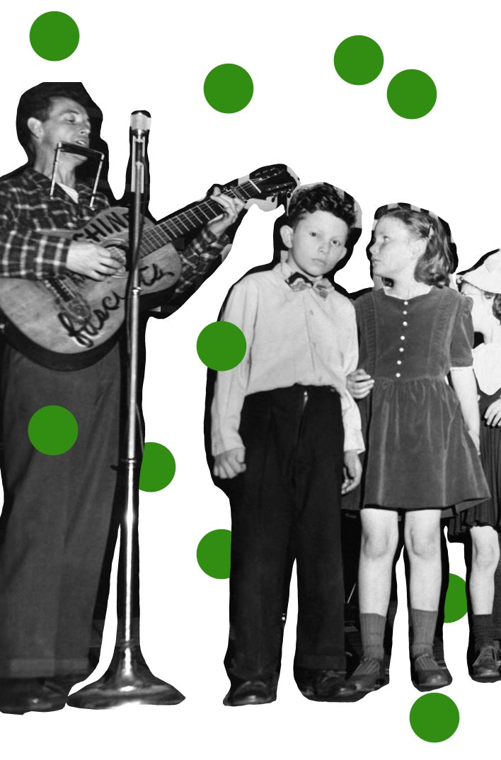 A black and white image of Woody Guthrie performing with a harmonica hanging and playing the guitar. The guitar has writing on it. Three kids are next to him watching him perform. There are green polka dots scattered over the image. 