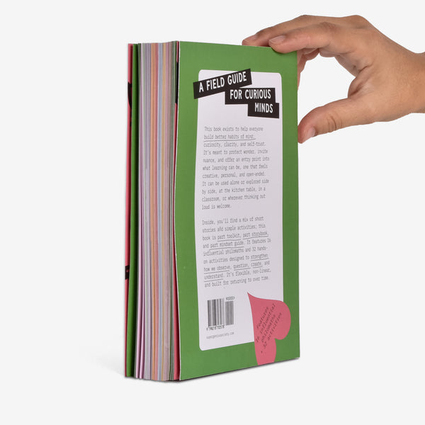 Hand holding a green book showing the back cover at an angle. The blurb title is 'A Field Guide for Curious Minds' on a white background