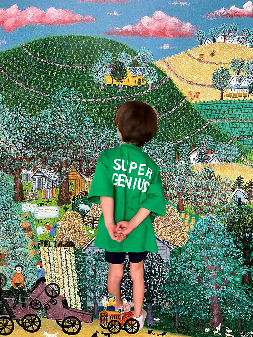 Child wearing a 'Super Genius' shirt standing in front of a colorful, detailed painted landscape.